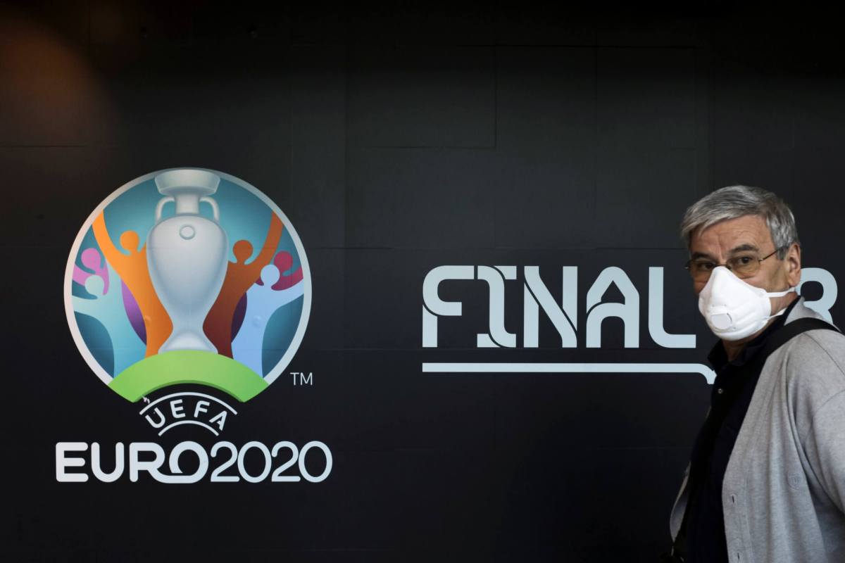 Travellers pass by a logo of the 2020 UEFA European Football Championship displayed on a wall inside Bucharest Henri Coanda International Airport