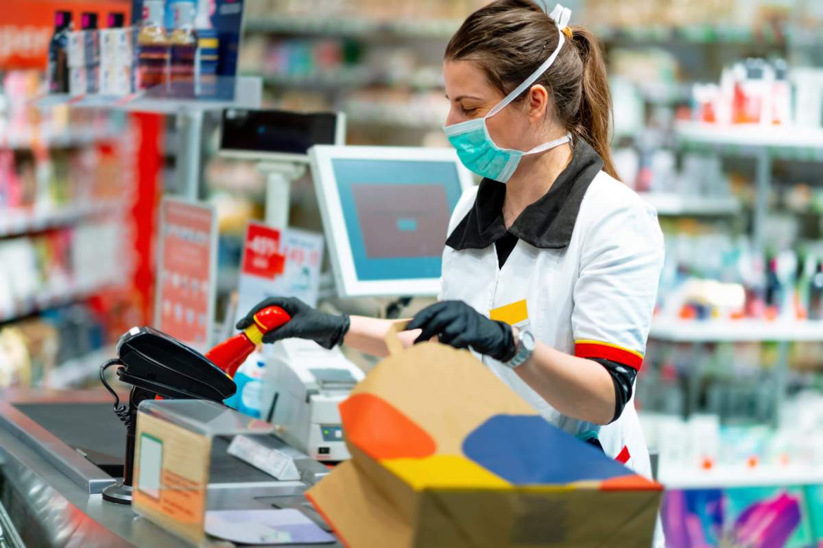 Woman cashier in mask and gloves working at the register