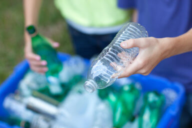 Hands placing bottles in recycling bin