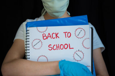 Close-up of student wearing face mask and surgical gloves, holding school books with Back to School written on cover