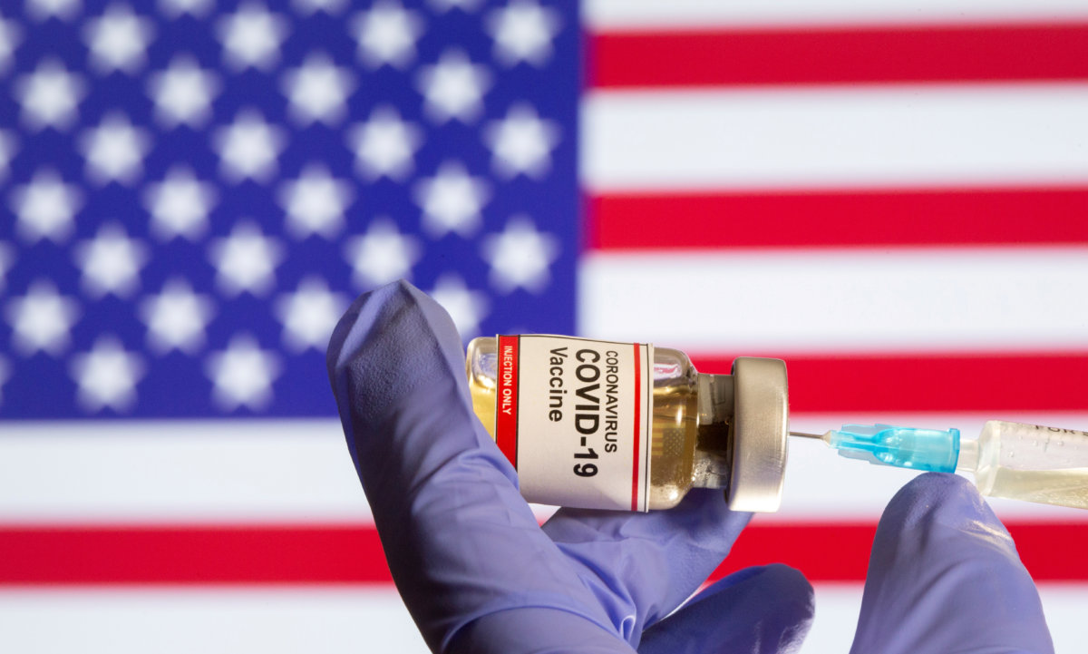 FILE PHOTO: A small bottle labeled with a “Coronavirus COVID-19 Vaccine” sticker and a medical syringe in front of displayed USA flag in this illustration