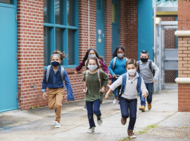 School children with face masks running outside building