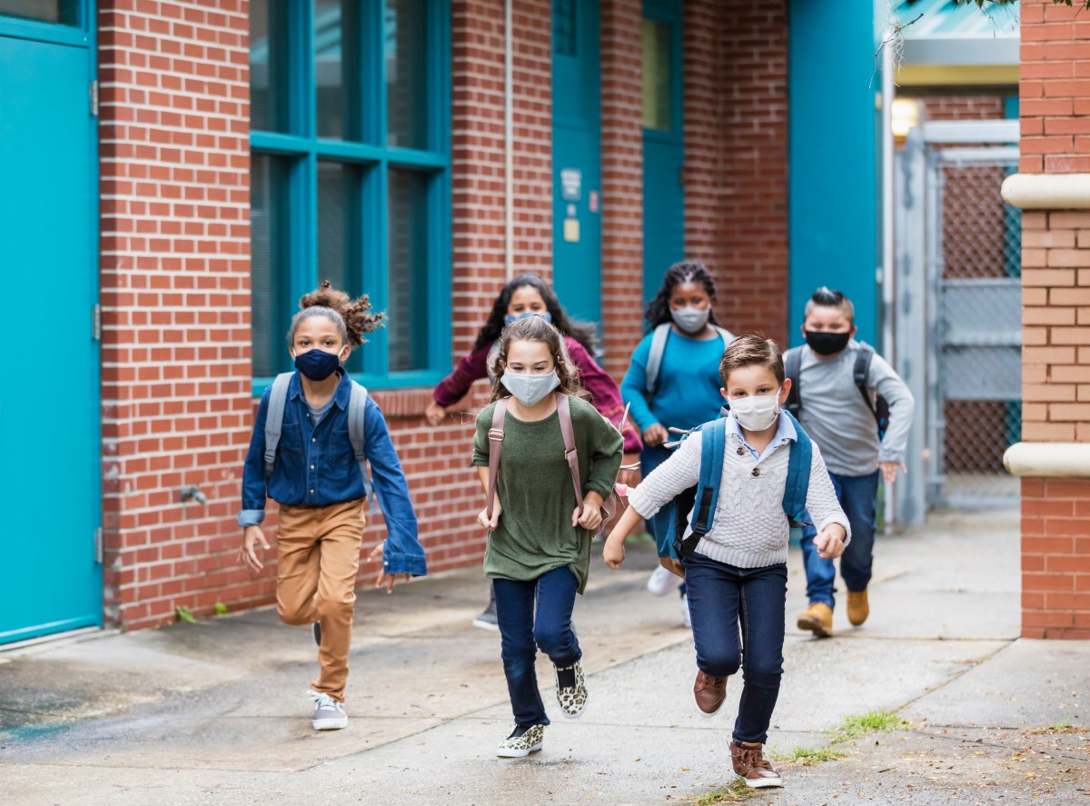 School children with face masks running outside building