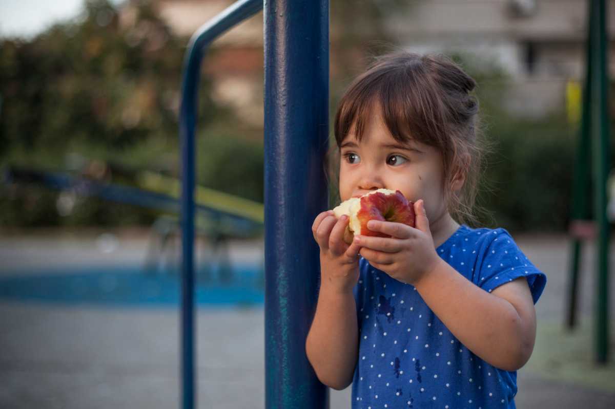Little girl eating apple at the playground