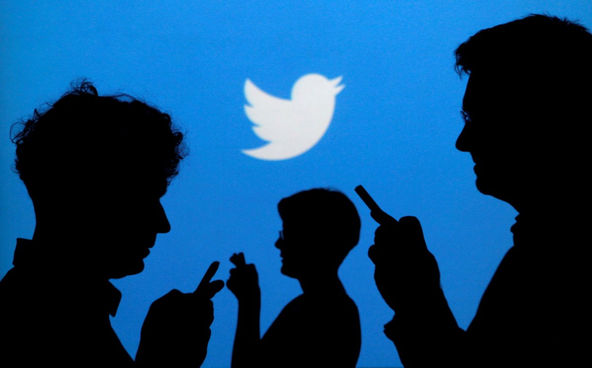 FILE PHOTO: People holding mobile phones are silhouetted against a backdrop projected with the Twitter logo  in Warsaw