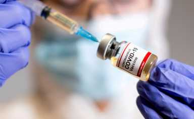 FILE PHOTO: A woman holds a medical syringe and a small bottle labelled “Coronavirus COVID-19 Vaccine