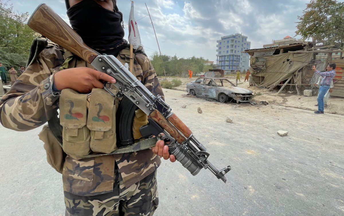 A member of Taliban forces stands guard as Afghan men take pictures of a vehicle from which rockets were fired, in Kabul