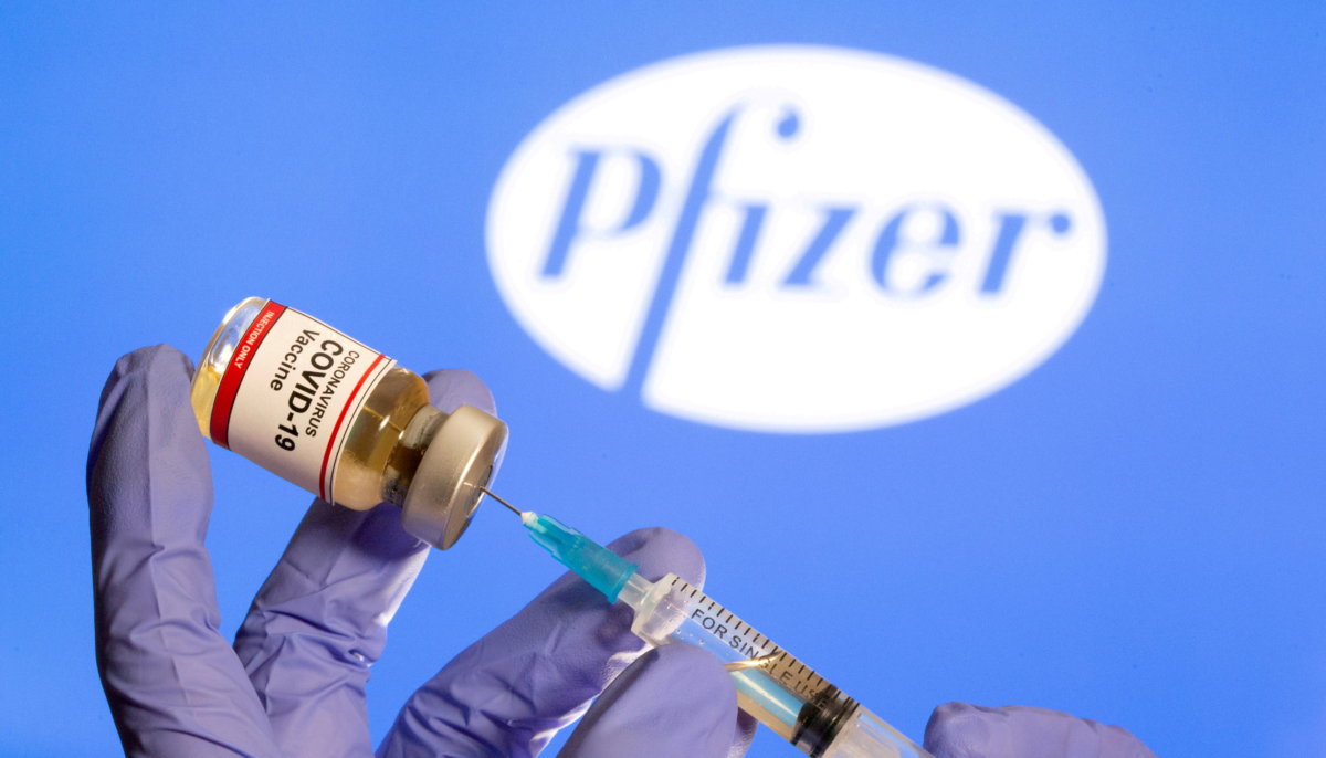 FILE PHOTO: A woman holds a small bottle labeled with a ‘Coronavirus COVID-19 Vaccine’ sticker and a medical syringe in front of displayed Pfizer logo in this illustration