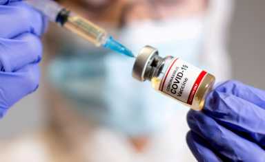 FILE PHOTO: A woman holds a medical syringe and a small bottle labelled “Coronavirus COVID-19 Vaccine