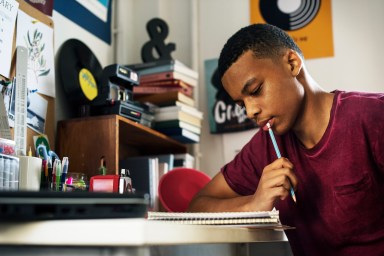 Teenage boy in a bedroom doing work thinking