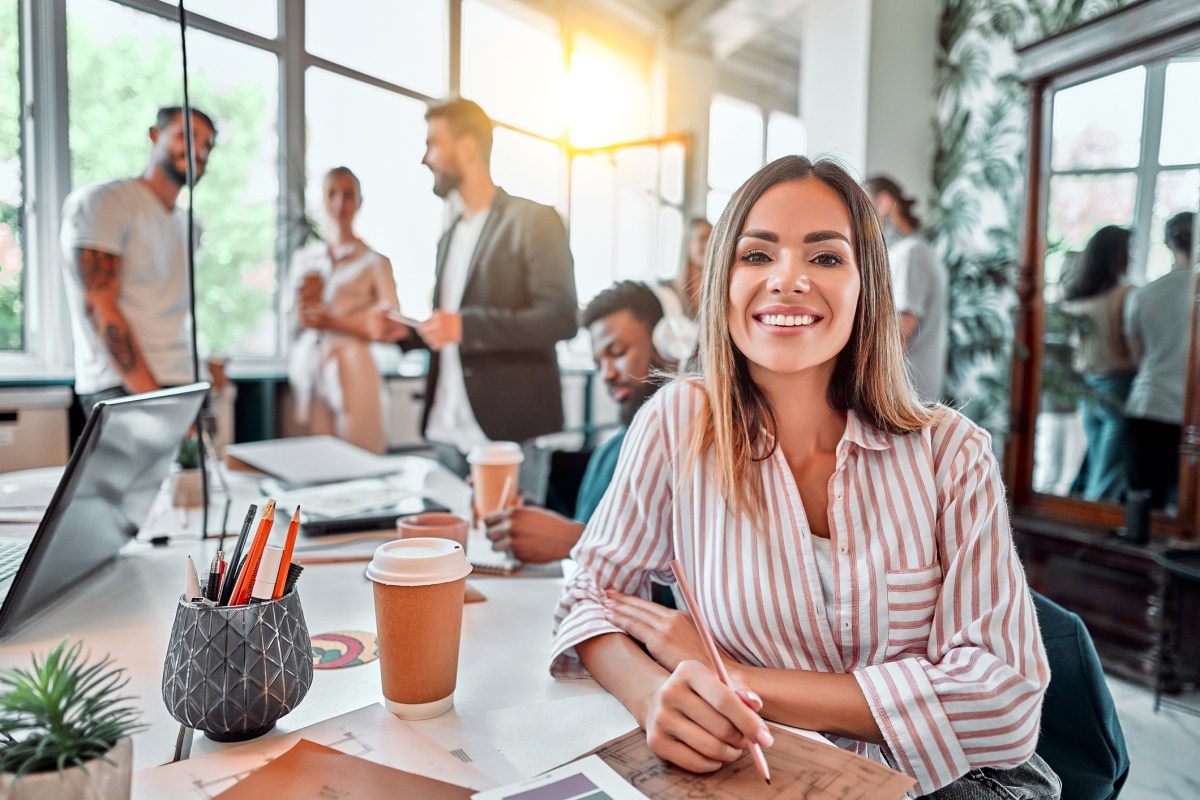 Smiling female employee sit in coworking space and working on the project