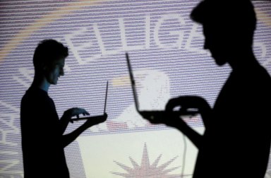 FILE PHOTO: People pose with laptops in front of projection of  binary code and CIA emblem in this picture illustration taken in Zenica