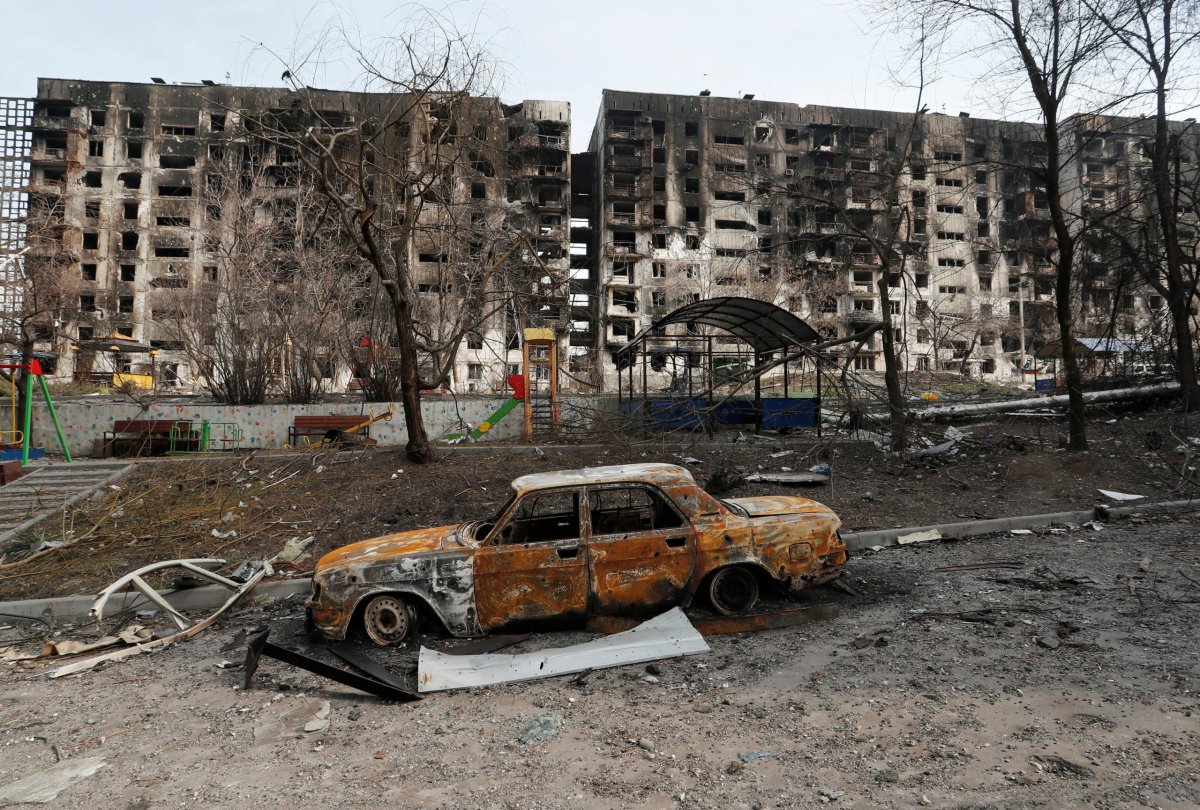 A charred car is seen in front of a destroyed apartment building in Mariupol