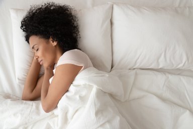 Serene calm african woman sleeping in comfortable bed, top view