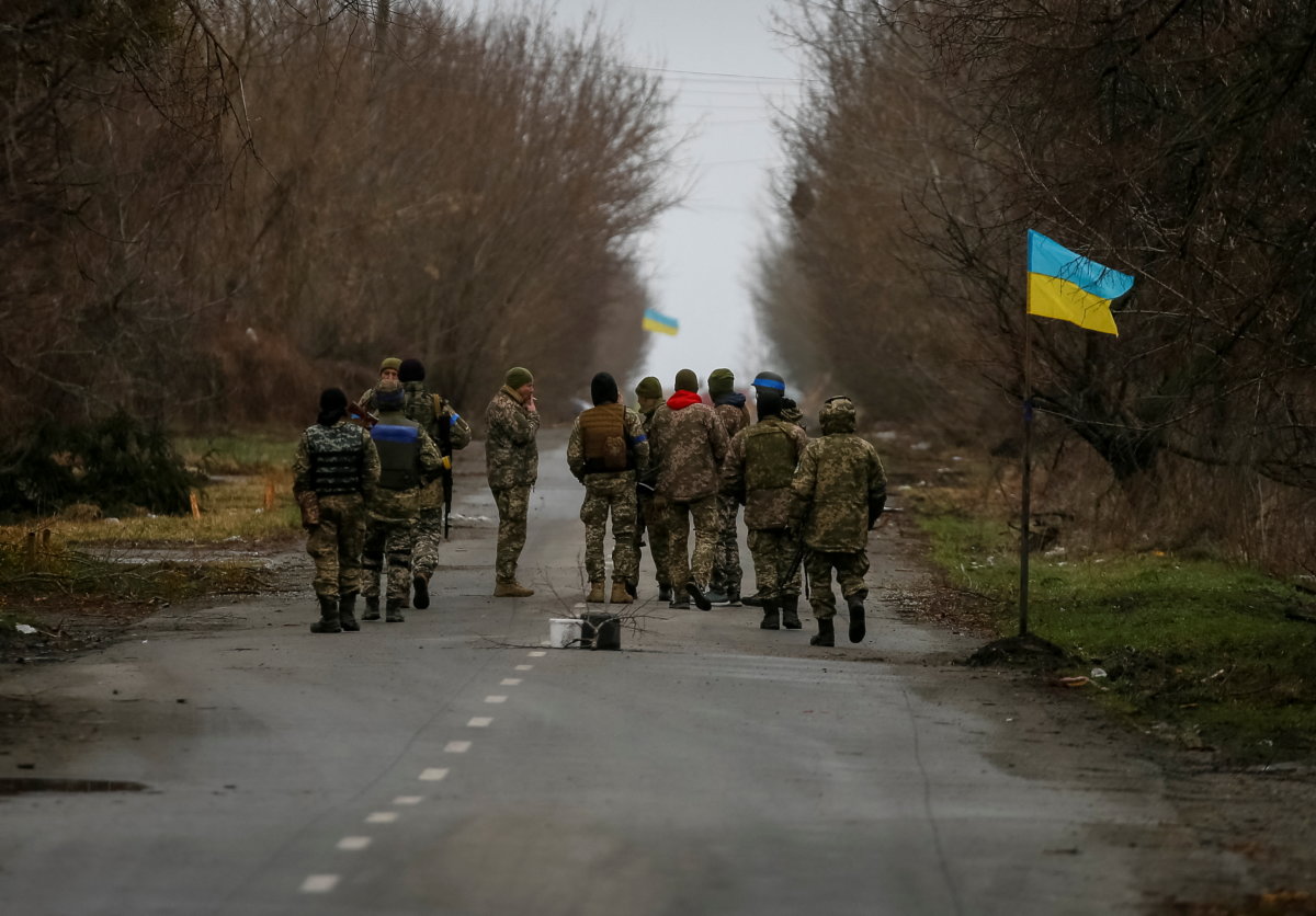 Ukrainian service members walk near a Ukrainian flag in the village of Kozarovychi