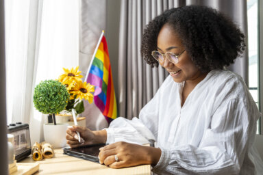 African American girl is working at home with LGBTQ rainbow flag in her table for coming out of closet and pride month celebration to promote sexual diversity and equality in homosexual orientation